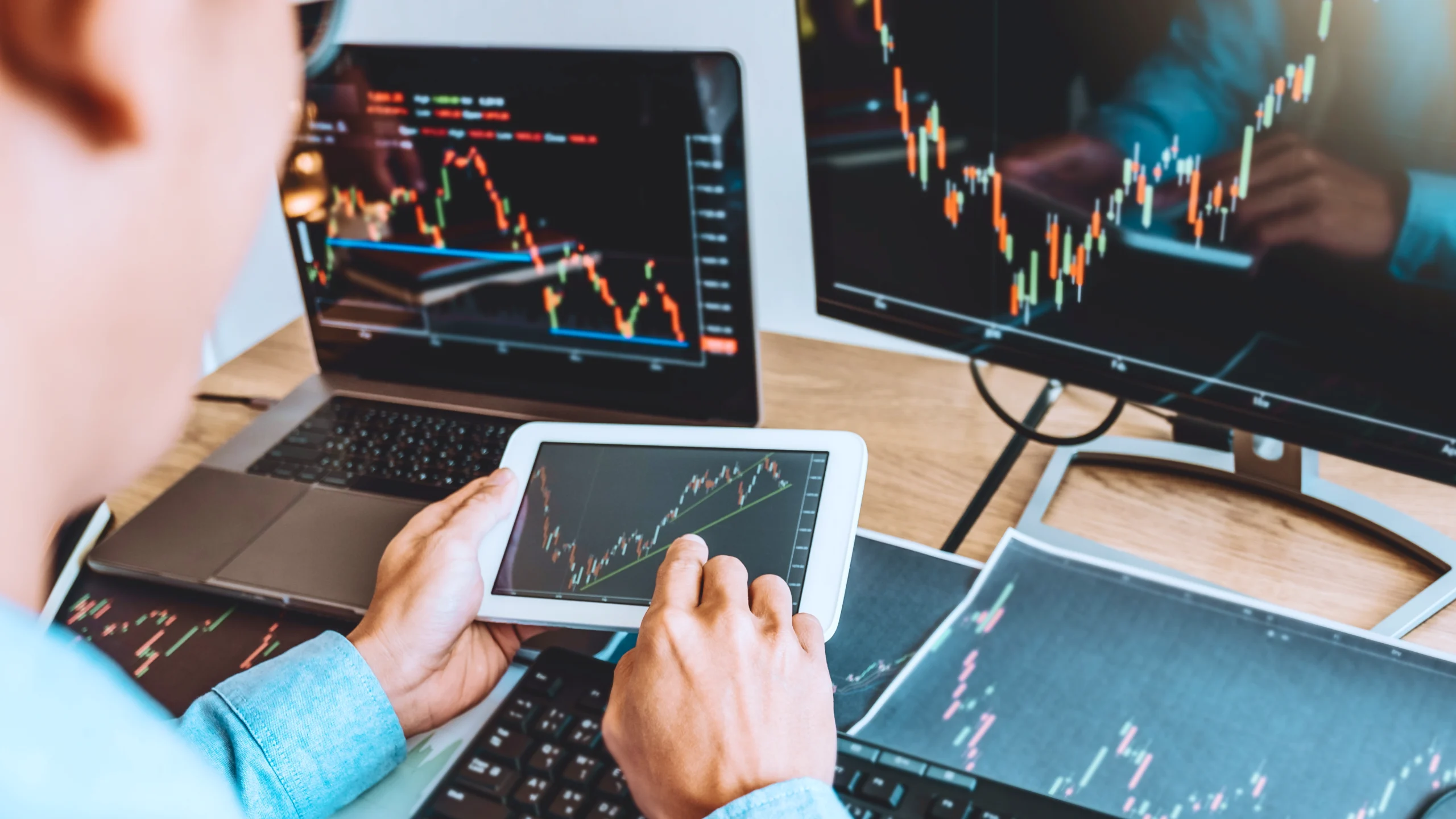 – PU Prime | More Than Trading man looking at pad, and his desk is full of papers, computer monitor and laptop, all of these are about the same cfd trading charts