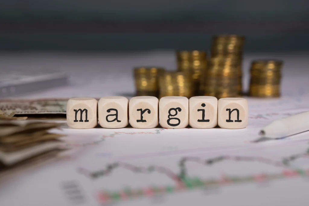 LYNXMPEB2F0YA_L – PU Prime | More Than Trading six small wooden cubes representing margin requirements concept, are placed in the background of currency, stock trends, etc.